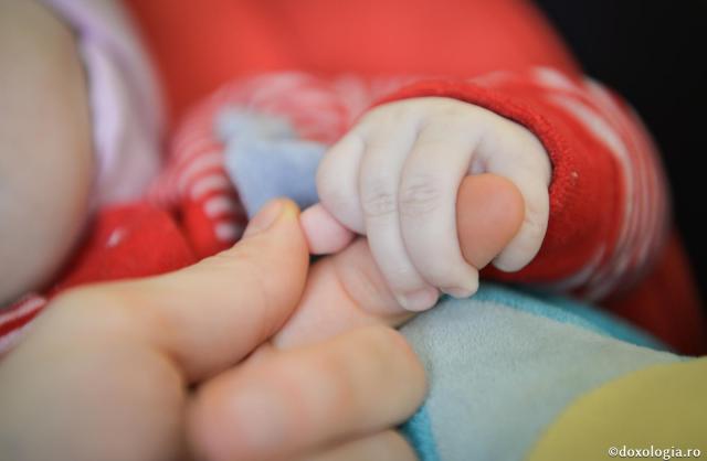 bebeluș ținând un deget în mână